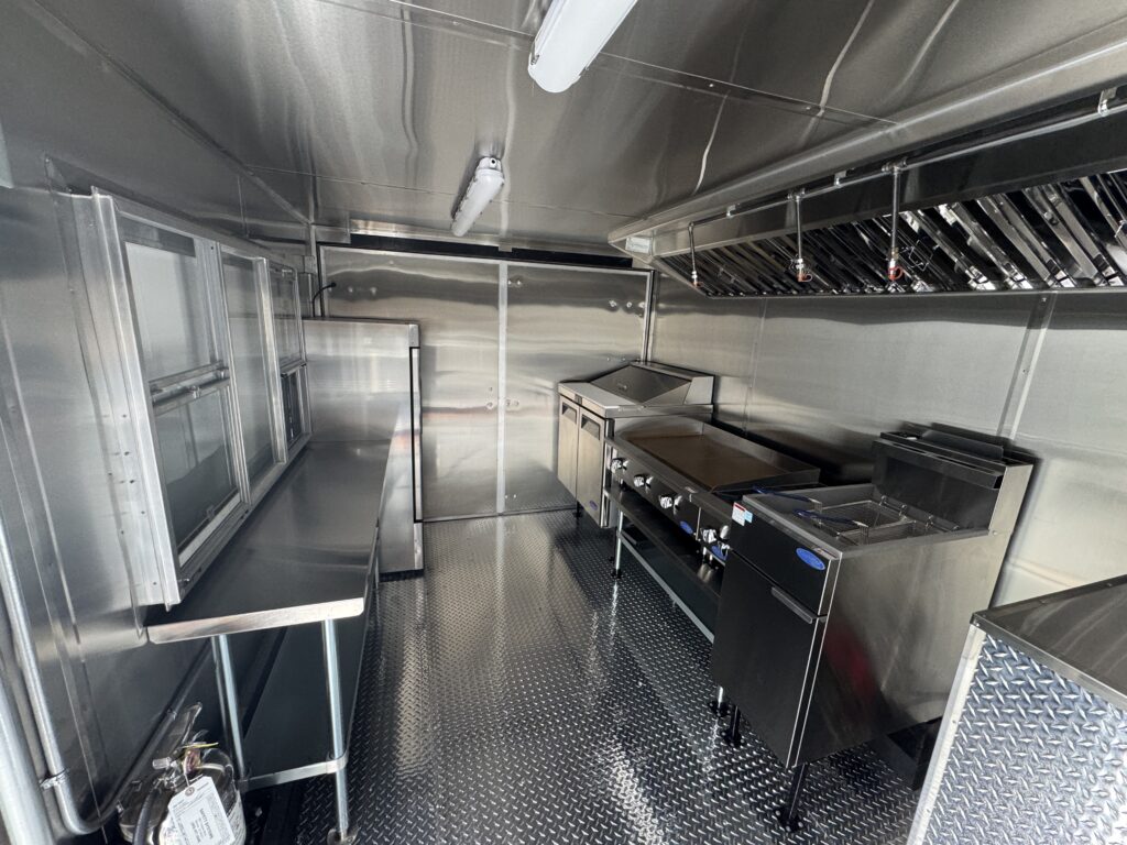 Stainless steel interior cook line of the Spur Catering food trailer with prep table, griddle, fryer, and reach-in refrigerator