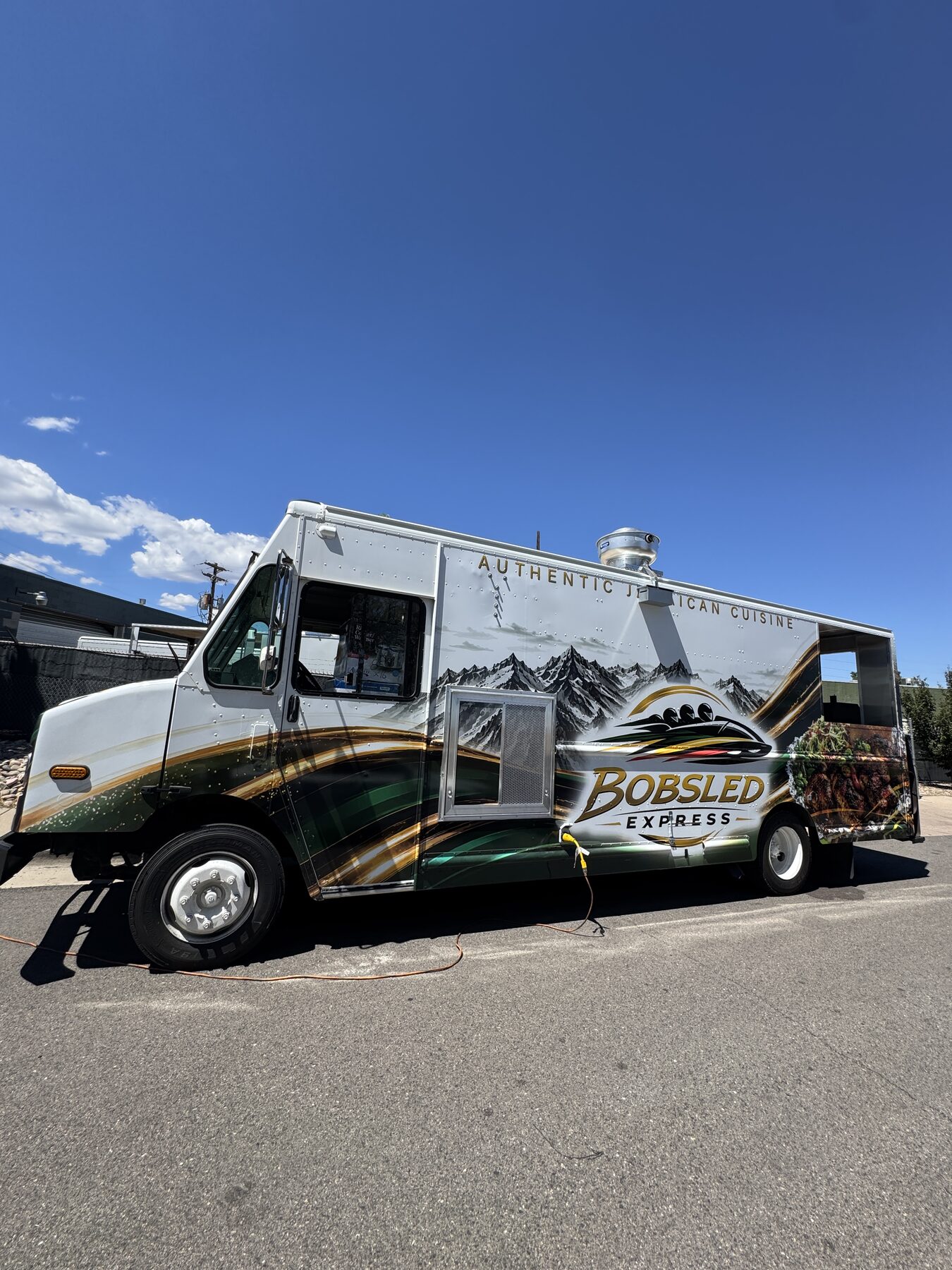 Green, gold and black wrap reading Authentic Jamaican Cuisine along the street side of the food truck