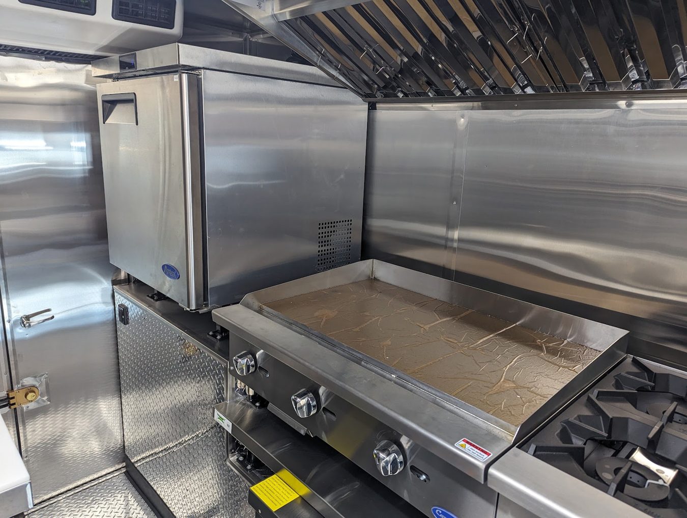 Thirty six inch griddle and two burner stove beside an undercounter refrigerator in the food truck cook line