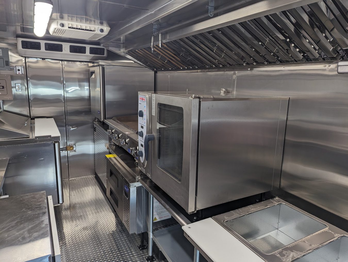 Combi oven on a stand under the exhaust hood inside the sixteen foot food truck