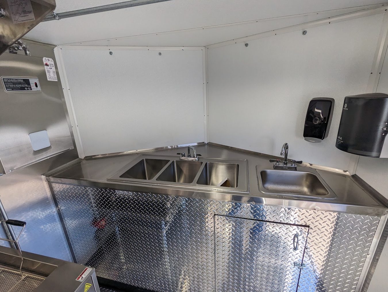 Three compartment sink and hand sink inside the tempura trailer with a towel dispenser on the wall