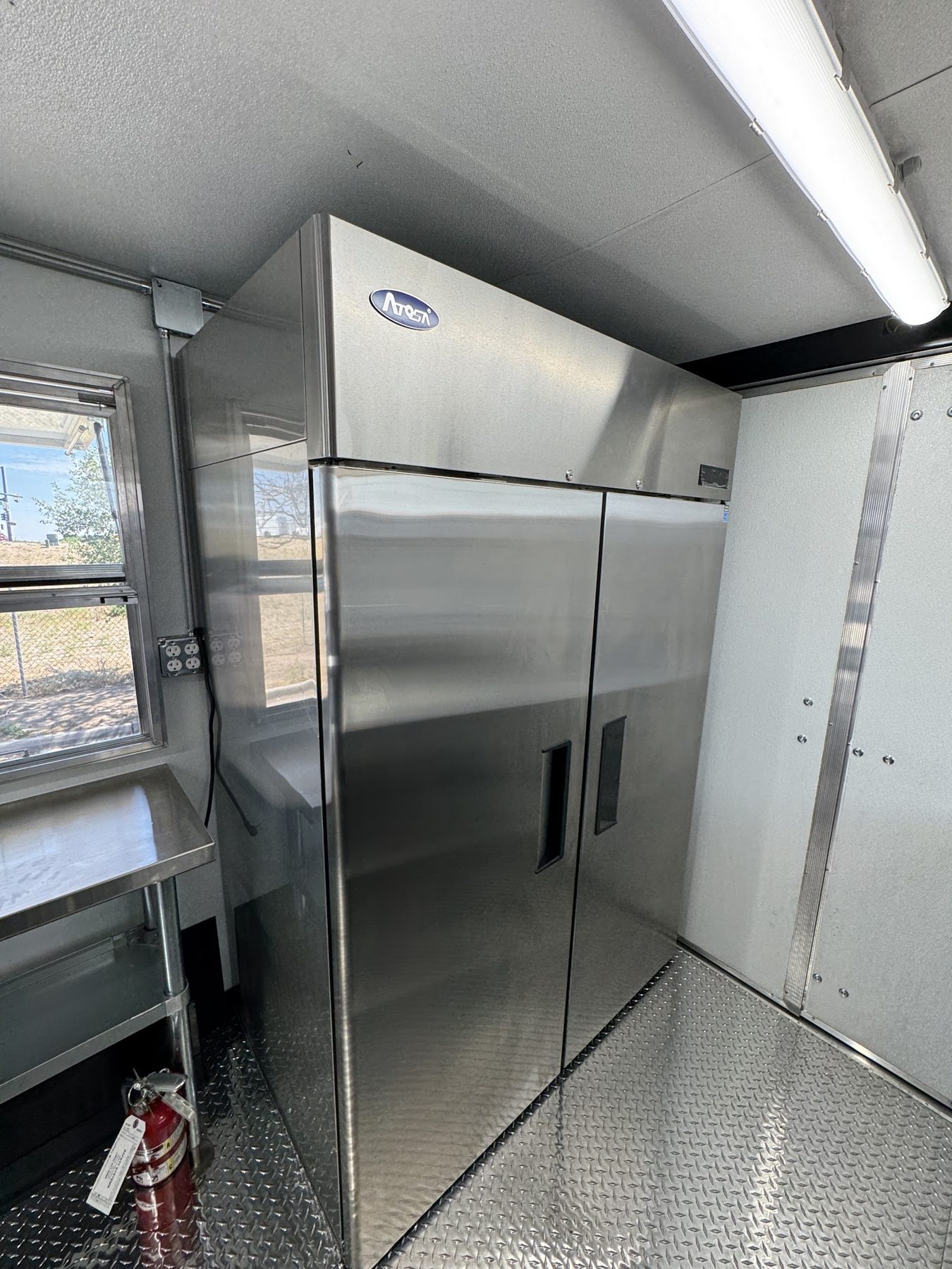 Atosa two door reach in refrigerator at the rear of the donut trailer with the fire extinguisher beside it